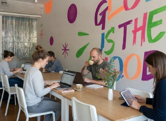 Papás trabajando con laptop en el coworking de WeGlow mientras sus hijos juegan en la ludoteca